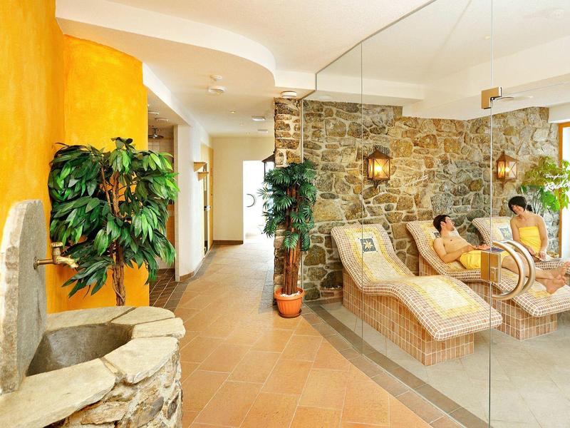 Gemütlicher Ruheraum mit Steinwand, Liegen, Pflanzen und warmem Licht in einem Spa-Bereich.