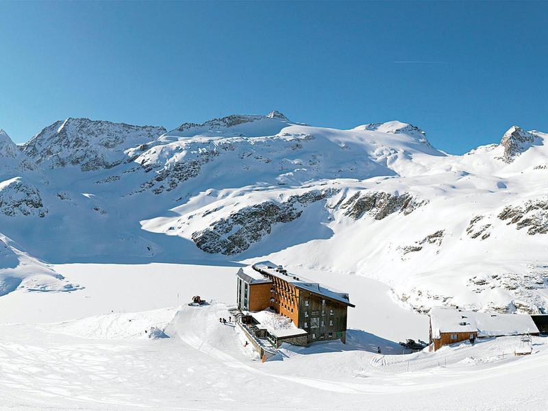 Einsames Chalet in verschneiter Berglandschaft unter klarem blauem Himmel.