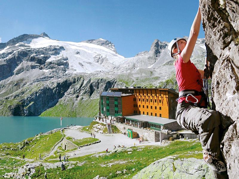 Frau klettert an Felsen nahe Bergsee und Hotel unter klarem blauem Himmel.