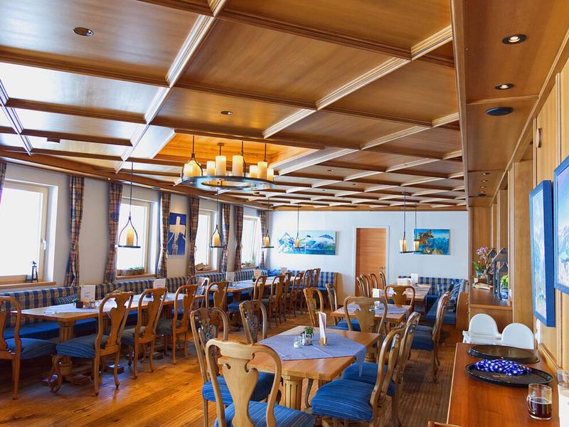 Großer Gastraum mit Holzmöbeln, blau gepolsterten Stühlen, Fenster und Deckenbeleuchtung.