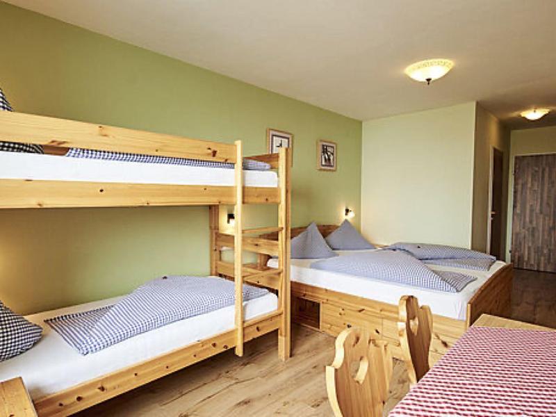 Schlafzimmer mit Etagenbett und Doppelbett, Holzmöbeln und grün gestrichenen Wänden.