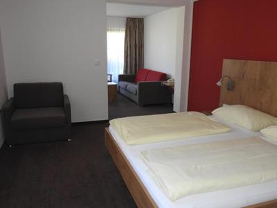 Une chambre d'hôtel simplement décorée avec deux lits, un fauteuil et un canapé près de la fenêtre.