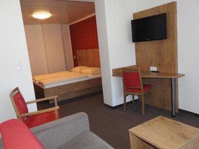 Chambre d'hôtel aménagée avec lit, deux chaises, bureau et télévision murale.