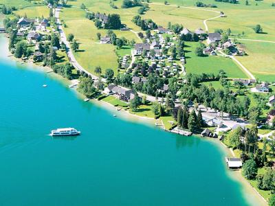 Vue aérienne d'un lac avec un bateau et un petit village sur la rive, entouré de champs verts.
