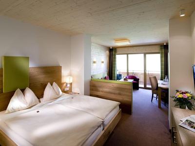 Gemütliches Hotelzimmer mit Doppelbett, Holzmöbeln, Balkon und Fernseher an der Wand.