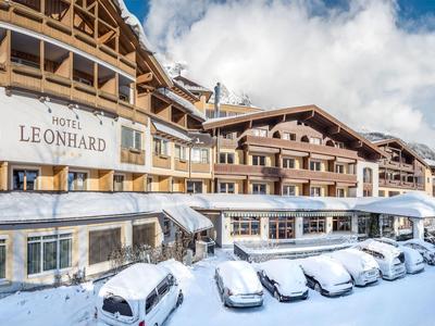 Hotel Leonhard s parkovištěm pokrytým sněhem a horami v pozadí pod jasnou oblohou