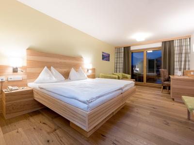 Helles Schlafzimmer mit Doppelbett, Holzboden, Nachttischen, Schreibtisch und großem Fenster mit Vorhängen.