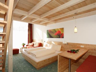 Helles Schlafzimmer mit Holzbett, grünem Teppich, Treppe und großem Fenster mit Vorhängen.