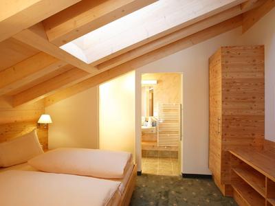 Gemütliches Schlafzimmer mit Holzbalken, Doppelbett, Lampe, Schrank und Fernseher unter Dachschräge.