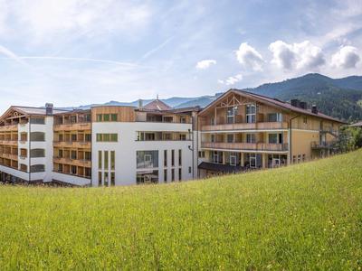 Großes Hotelgebäude vor grüner Wiese und bewaldeten Bergen unter blauem Himmel mit Wolken.