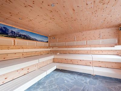 Helle Sauna mit mehrstufigen Holzbänken, Holzverkleidung und Steinboden, Panorama-Dekor an Wand.