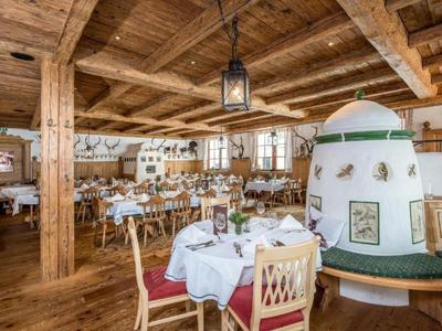Rustikales Restaurant mit Holzdecke, weißen Tischdecken, gemütlichem Kachelofen und Holzmöbeln.
