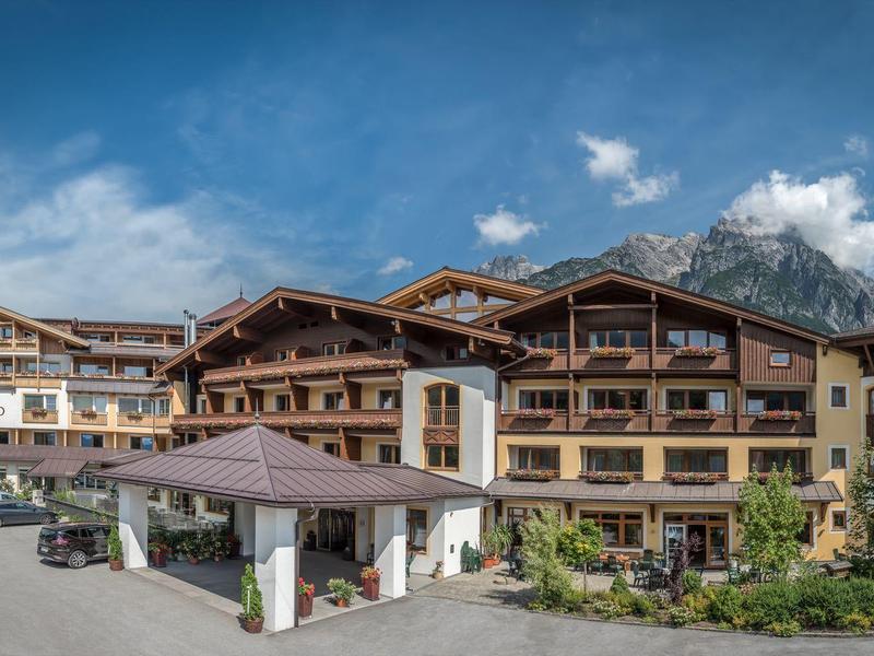 Großes Alpenhotel mit Holzverkleidung in landschaftlicher Bergkulisse bei sonnigem Himmel