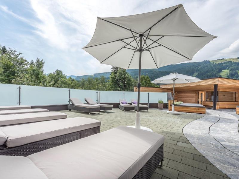 Dachterrasse mit weißen Sonnenschirmen, grauen Liegestühlen und Holzhütte bei bewölktem Himmel.