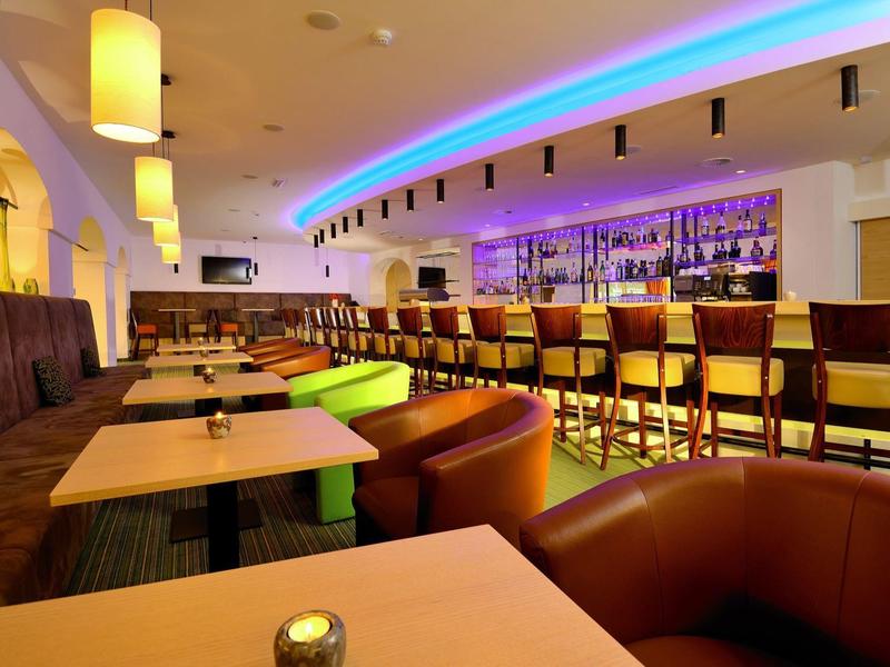 Moderne Hotelbar mit beleuchtetem Tresen und bequemen Stühlen in warmem Ambiente.