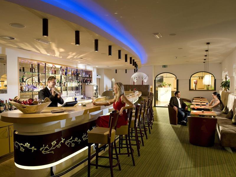 Moderne Hotelbar mit geschwungenem Tresen, Barhockern und entspannter Atmosphäre.