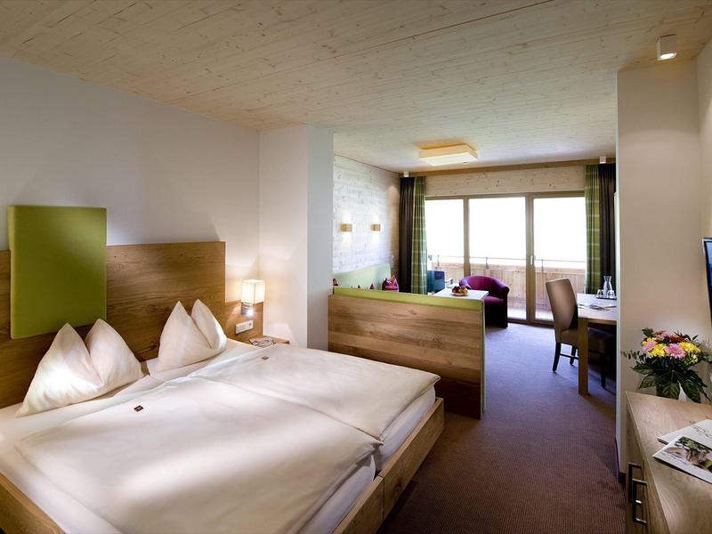 Gemütliches Hotelzimmer mit Doppelbett, Holzmöbeln, Balkon und Fernseher an der Wand.