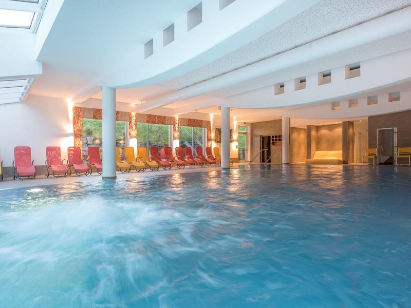 Innen-Schwimmbad mit blauem Wasser, vielen rot-gelben Liegestühlen und weißer Decke.