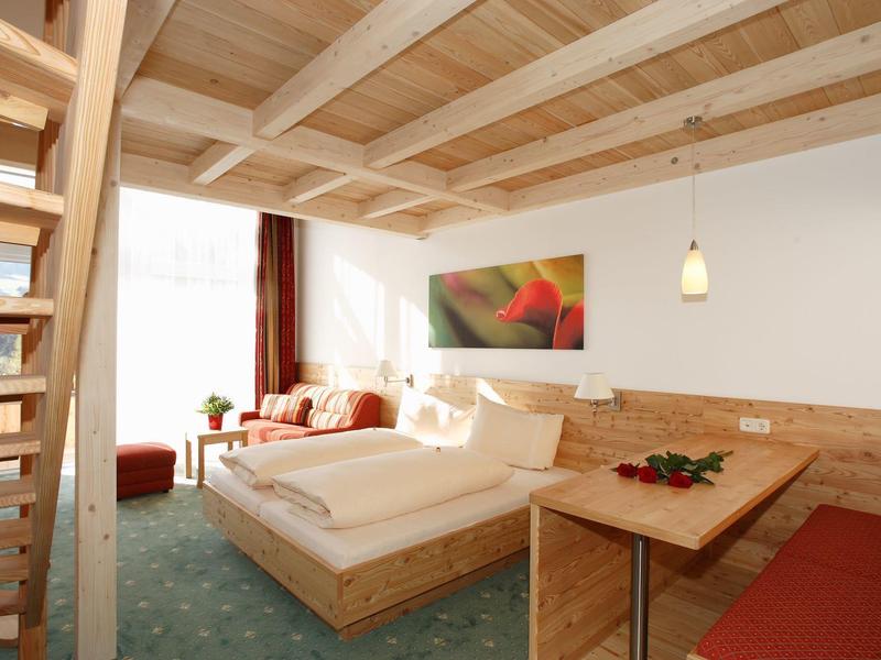 Helles Schlafzimmer mit Holzbett, grünem Teppich, Treppe und großem Fenster mit Vorhängen.