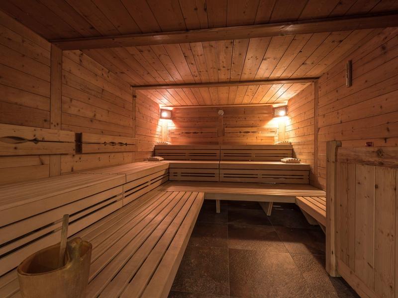 Gemütliche Sauna mit Blockholzwänden, Holzbänken, Beleuchtung und Saunakübel.