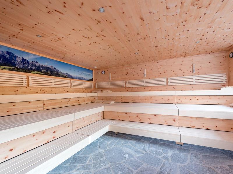 Helle Sauna mit mehrstufigen Holzbänken, Holzverkleidung und Steinboden, Panorama-Dekor an Wand.