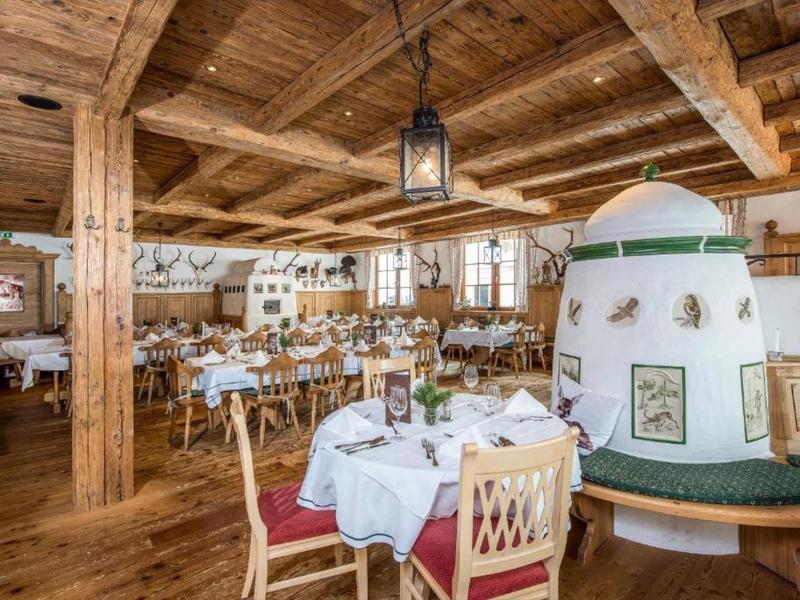 Rustikales Restaurant mit Holzdecke, weißen Tischdecken, gemütlichem Kachelofen und Holzmöbeln.