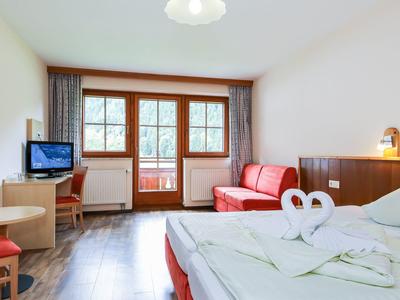 Chambre d'hôtel lumineuse avec lit double, canapé rouge, bureau et balcon avec vue sur la verdure.
