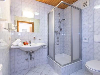 Salle de bain lumineuse avec douche, lavabo, toilettes et grands carreaux blancs.