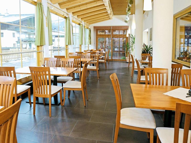 Salle à manger lumineuse avec chaises en bois et grandes fenêtres donnant sur l'extérieur.