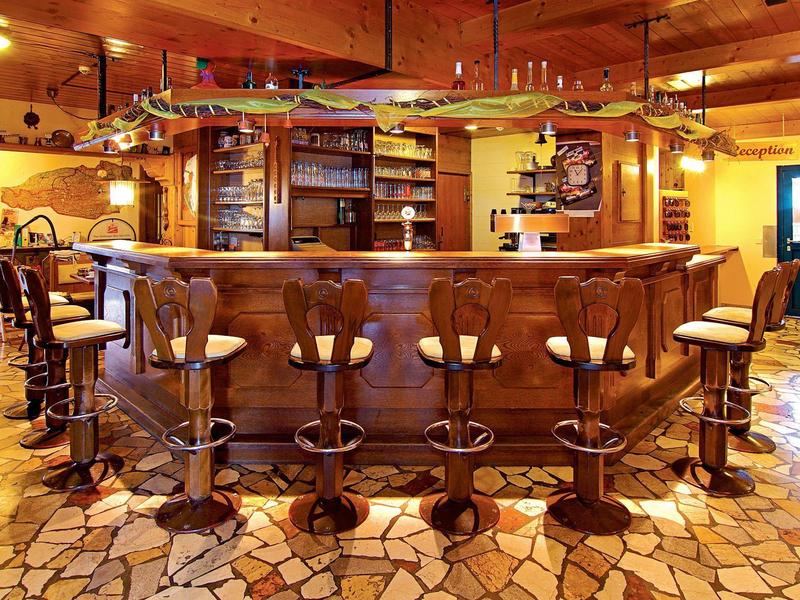 Bar d'hôtel rustique avec comptoir en bois et tabourets sur sol en pierre.