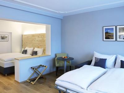 Habitación de hotel moderna con dos camas dobles, paredes azules y decoración mínima.