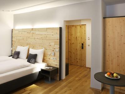 Habitación de hotel moderna con cama doble, detalles de madera y una pequeña mesa con fruta.