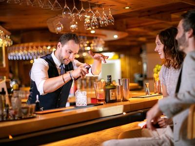 Barman prepara un cóctel para dos clientes en un bar acogedor con decoración de madera.
