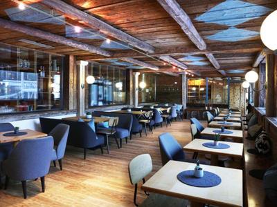 Área de restaurante acogedora con suelos de madera, vigas en el techo y mobiliario moderno.