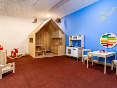 Zona de juegos infantil luminosa con muebles de madera, cocina de juguete y alfombra roja en un área de hotel.