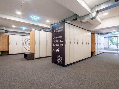 Área de vestuario moderna con taquillas de madera, alfombra gris y bancos en un hotel.