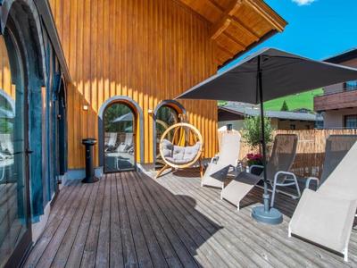 Terraza con tumbonas, silla colgante y sombrilla frente a casa de madera bajo cielo despejado.