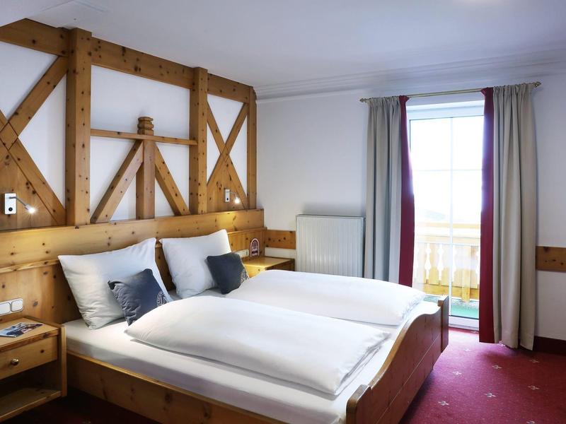 Habitación de hotel acogedora con cama doble, elementos de madera y balcón con luz natural.