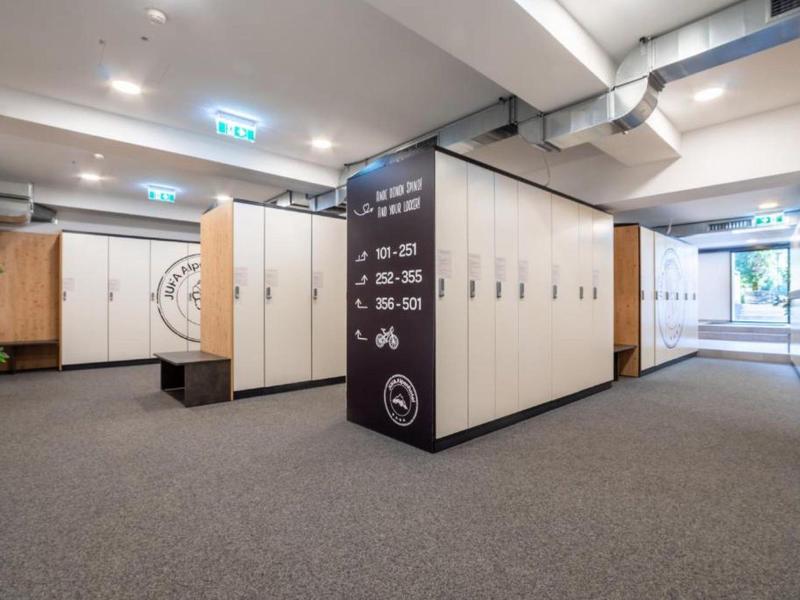 Área de vestuario moderna con taquillas de madera, alfombra gris y bancos en un hotel.