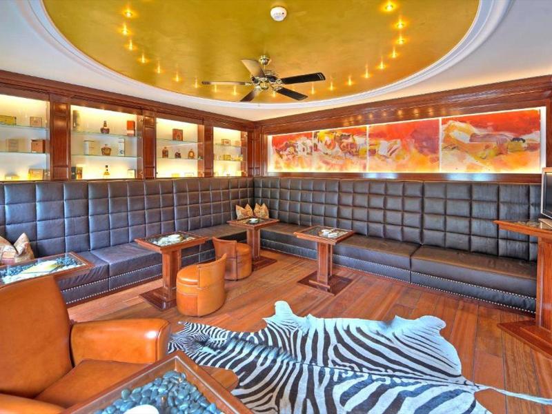 Una elegante sala de hotel con sillones de cuero, sofá integrado y alfombra de piel de cebra sobre suelo de madera.