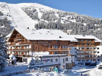 Snow-covered hotel building in a mountain landscape with clear blue sky.
