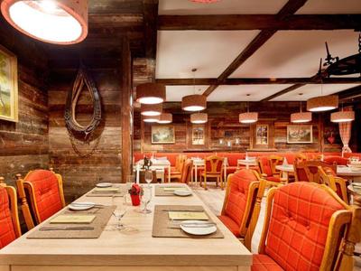 Gemütlicher, rustikaler Speisesaal mit Holzverkleidung und orangen gepolsterten Stühlen.