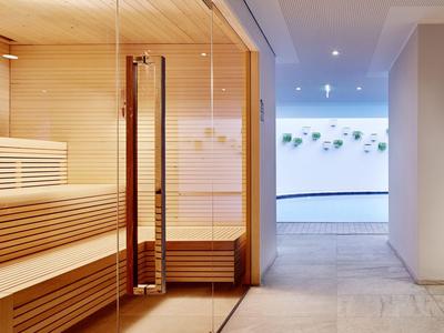 Modern sauna room with wooden benches and glass wall next to a brightly lit corridor.