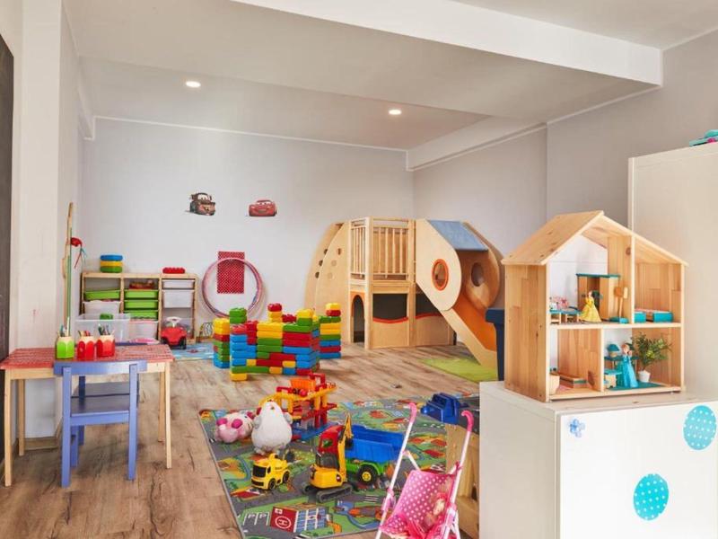 Colorful children's playroom with wooden playhouses, tables, chairs, and toys.