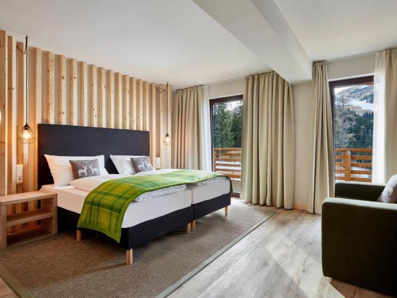 Modern hotel room with double bed, wooden paneling, and nature view.
