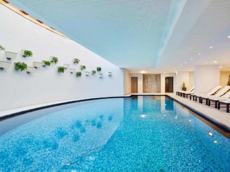 Modern indoor pool with cozy lounge chairs and wall greenery in a hotel.