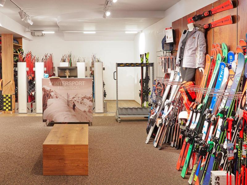 Interior with skis lined up on the right wall and a luggage cart in a hotel or winter sports facility.