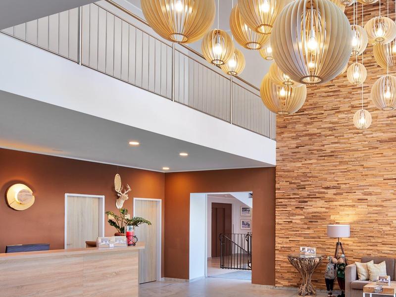 Modern hotel lobby with wooden reception desk, hanging lights, and cozy seating area.