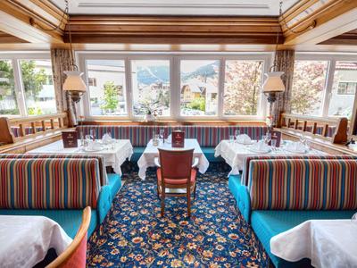 Helles Restaurant mit großen Fenstern, gemustertem Teppich und gestreiften Sitzbänken.