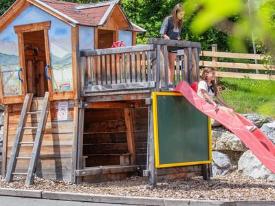 Hrací domek s klouzačkou a malovanou fasádou v hotelovém venkovním prostoru
